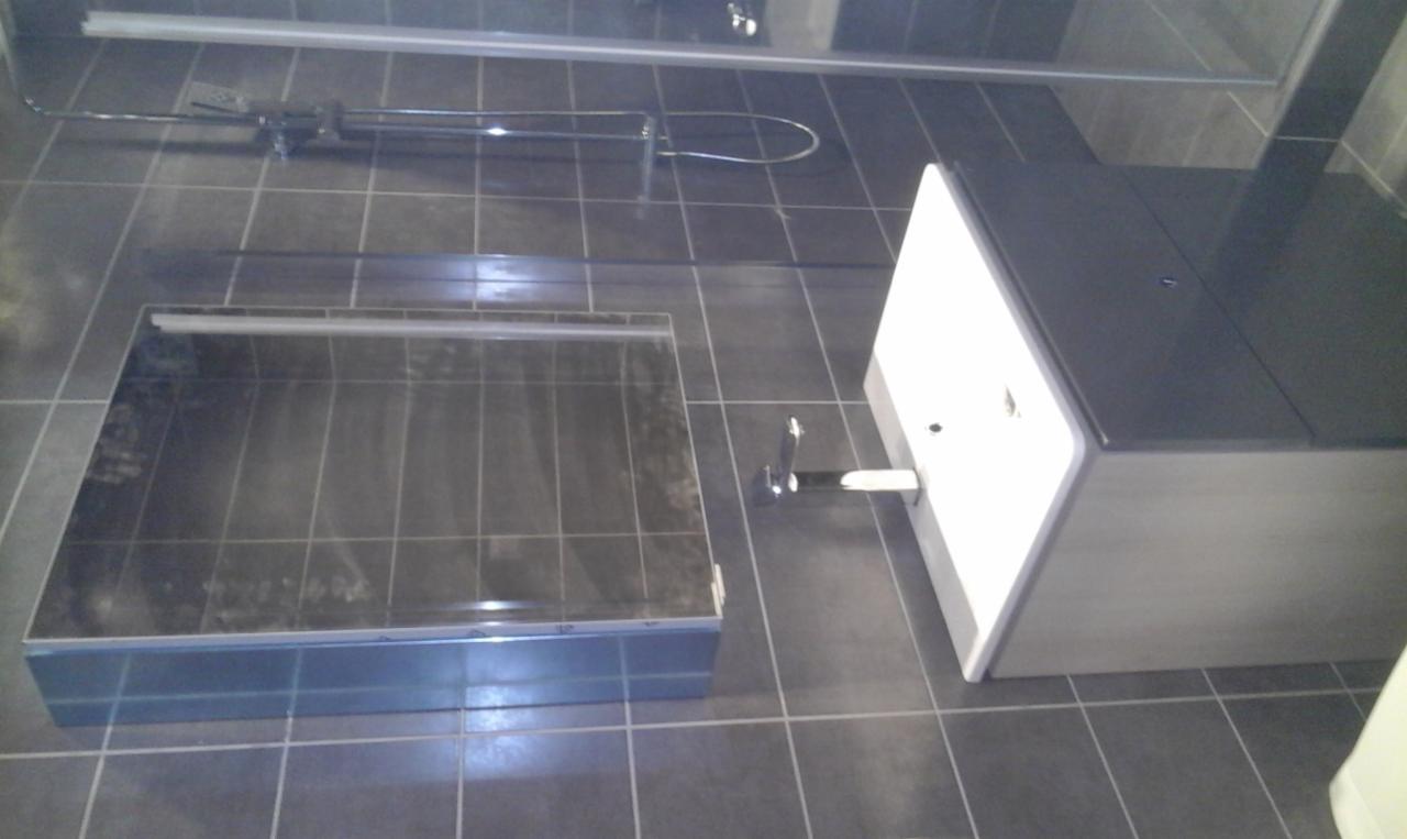 Nowoczesna łazienka z ciemnymi płytkami podłogowymi, brodzikiem z niskim progiem i białą szafką umywalkową z chromowaną baterią.