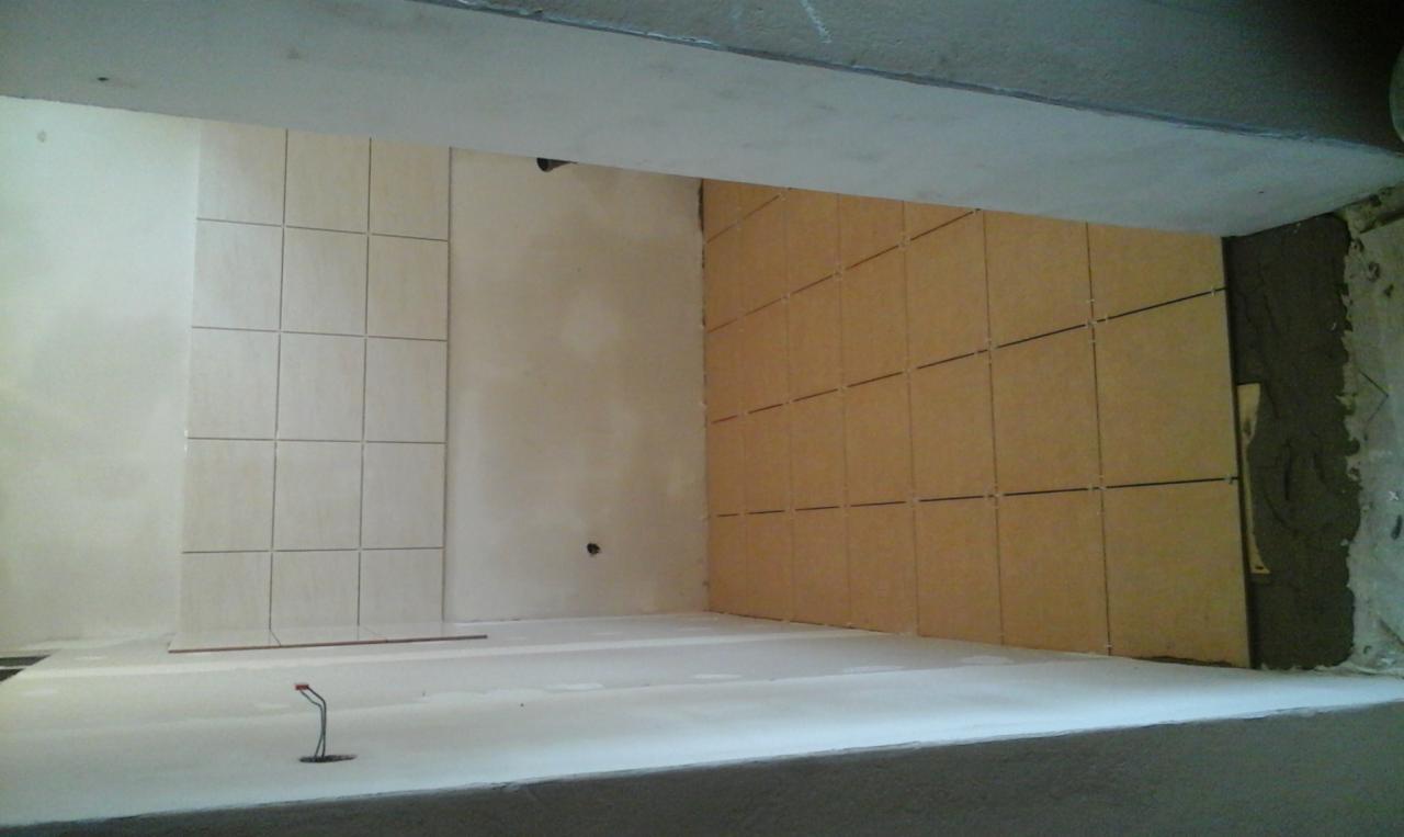 Montaż płytek ceramicznych na ścianie, widoczne płytki w dwóch kolorach, jasne i beżowe, z fugami, częściowo położone, z pozostawionymi szczelinami dylatacyjnymi, widoczna zaprawa klejowa na ścianie.