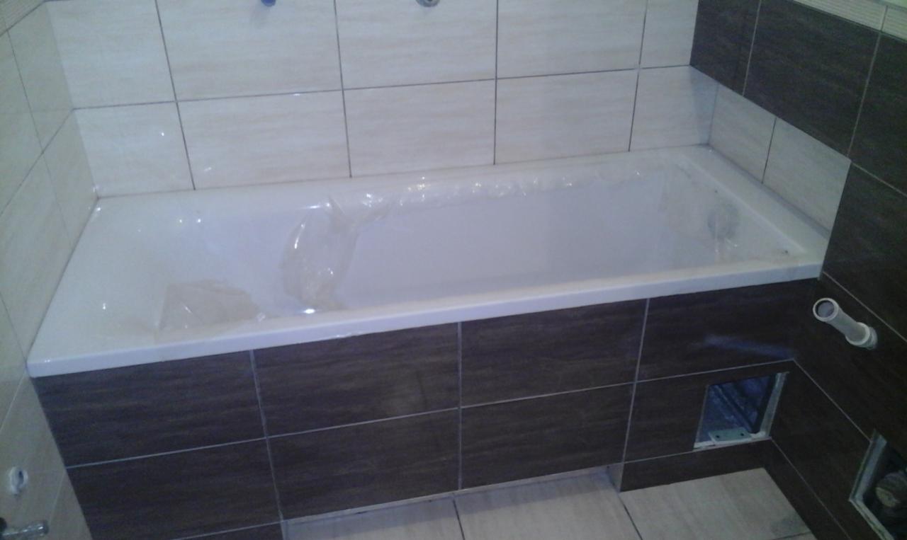 Nowa wanna obudowana brązowymi i beżowymi płytkami, zabezpieczona folią ochronną, widoczny otwór rewizyjny.