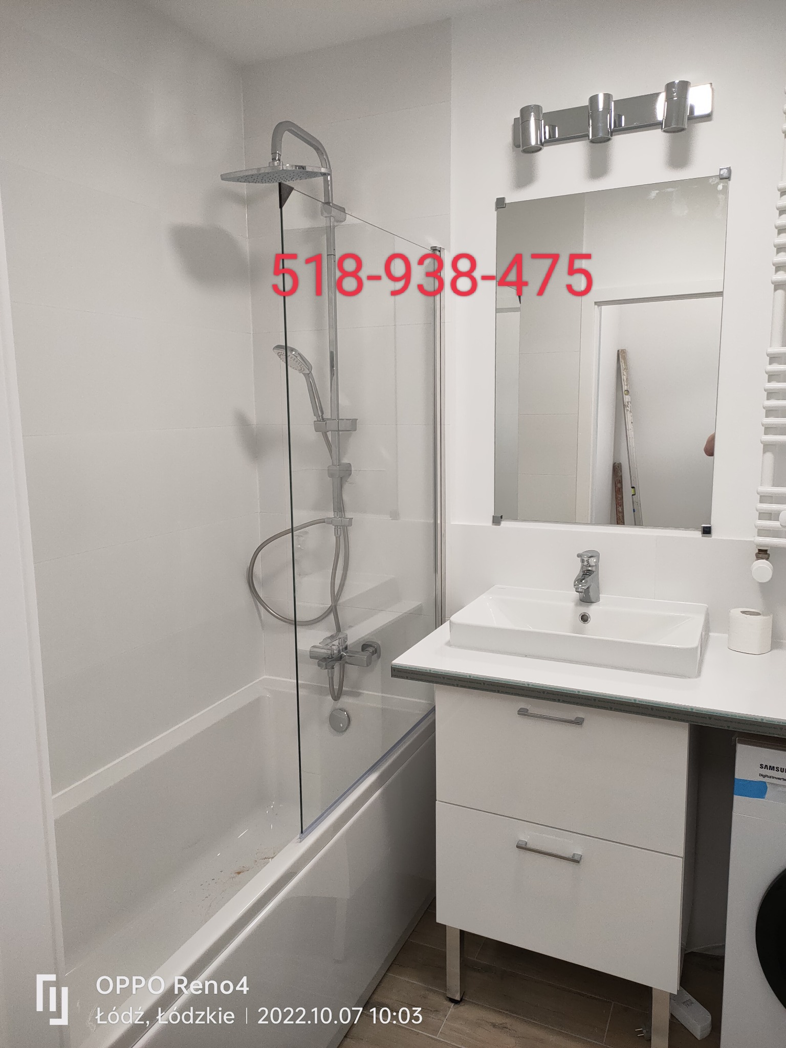 Biała łazienka po remoncie z kabiną prysznicową, umywalką w szafce i grzejnikiem drabinkowym, widoczne płytki na ścianach i pralka z boku.