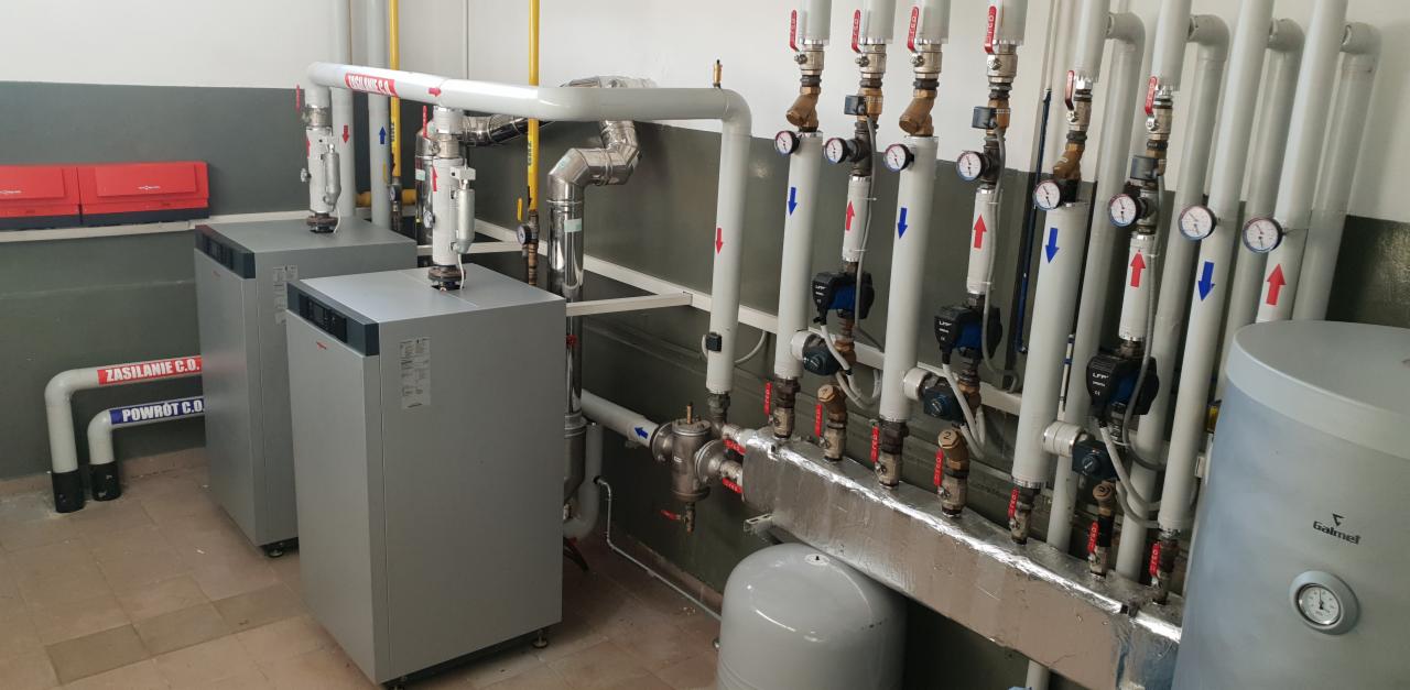 Kotłownia w Krobi: Dwa szare kotły grzewcze Viessmann z podłączonymi rurami oznaczonymi strzałkami, obok biały zasobnik Galmet, instalacja centralnego ogrzewania.