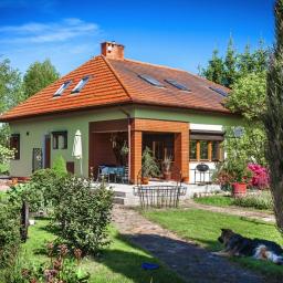 Bautyk - Parterowy dom z czerwoną dachówką i oknami dachowymi, widok z ogrodu z leżącym psem na pierwszym planie.
