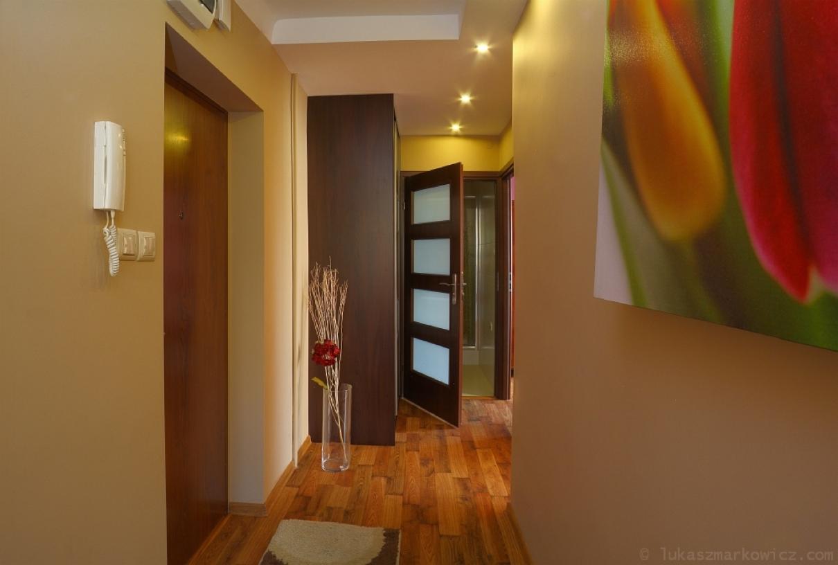 Wnętrze przedpokoju z drewnianą podłogą, drzwiami wewnętrznymi z przeszkleniami i dekoracyjną grafiką kwiatową na ścianie.