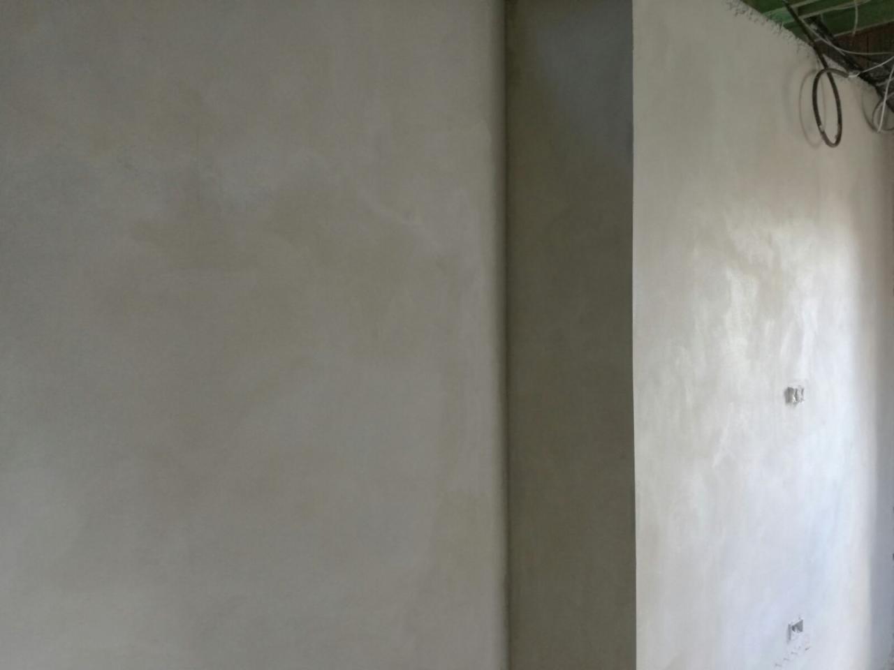 Świeżo położone, gładkie tynki maszynowe w odcieniach szarości, widoczne kable i puszki elektryczne, surowy stan wykończenia wnętrza.