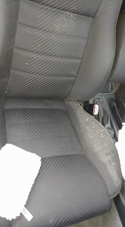 Brudny, czarny fotel samochodowy z widocznymi plamami i zabrudzeniami na tapicerce oraz białą szmatką do czyszczenia.