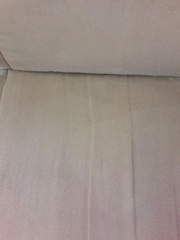 Zbliżenie na jasną tapicerkę sofy z widocznym, delikatnym wzorem tkaniny i niewielkim zabrudzeniem.