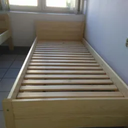 Surowy, sosnowy stelaż łóżka jednoosobowego z listewkami, widok z góry, w tle okno z zasłonami.