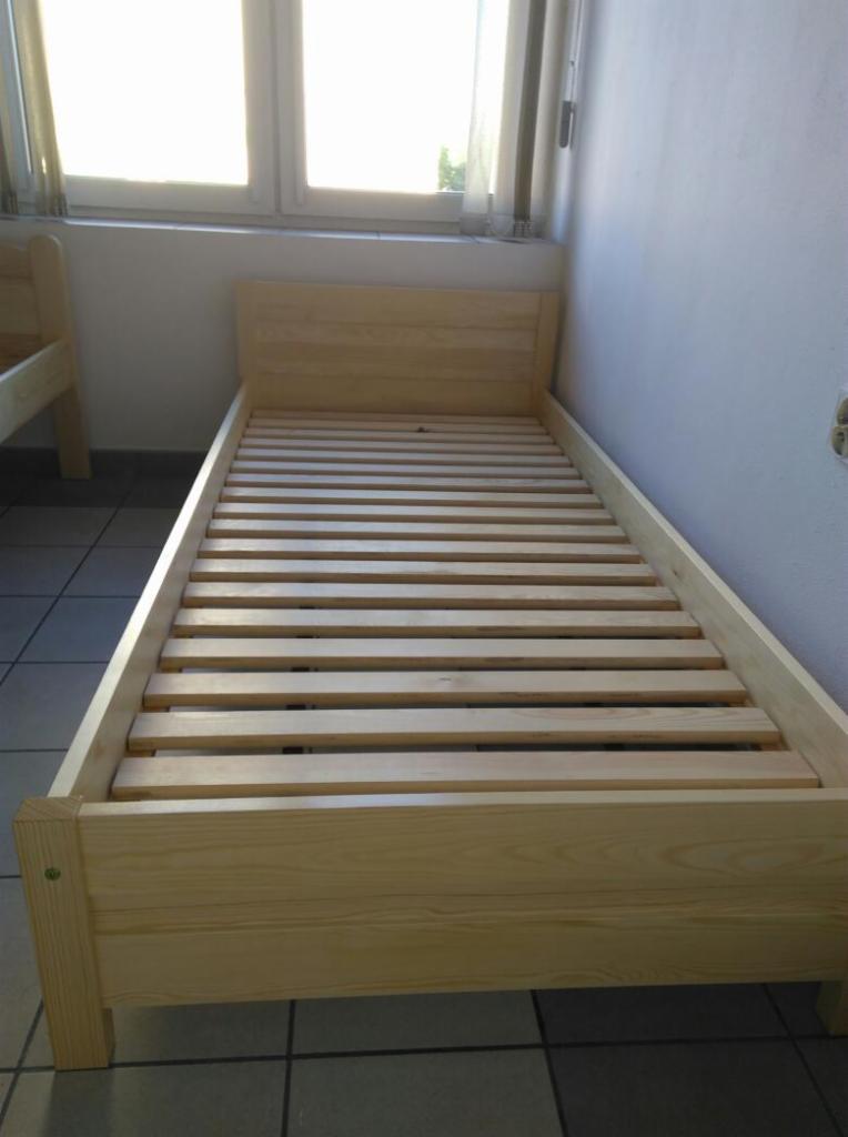 Surowy, sosnowy stelaż łóżka jednoosobowego z listewkami, widok z góry, w tle okno z zasłonami.