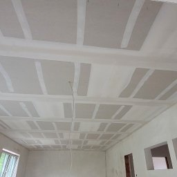 Gfk Design Grzegorz Kowalski - Sufit po montażu płyt karton-gips, z widocznymi łączeniami i szpachlowaniem. Widok z dołu ukazuje regularną strukturę i przygotowanie do dalszych prac wykończeniowych.
