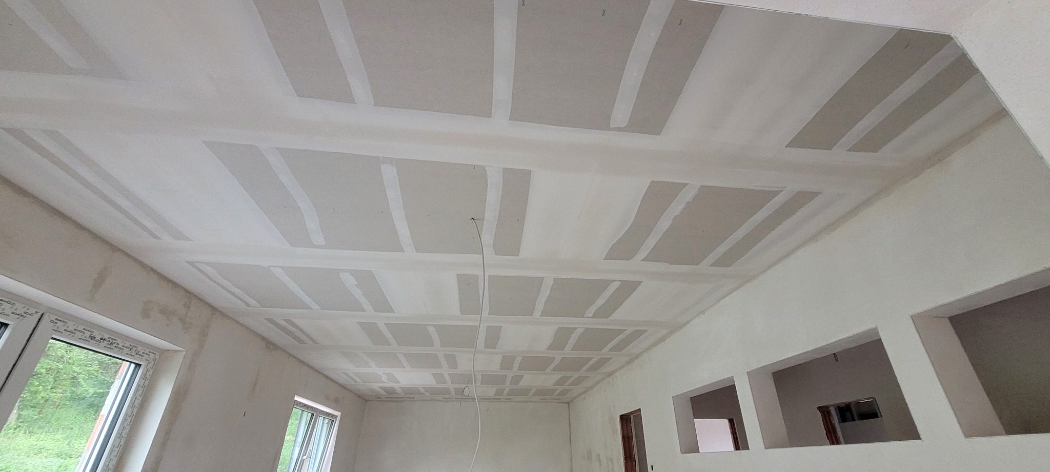 Sufit po montażu płyt karton-gips, z widocznymi łączeniami i szpachlowaniem. Widok z dołu ukazuje regularną strukturę i przygotowanie do dalszych prac wykończeniowych.