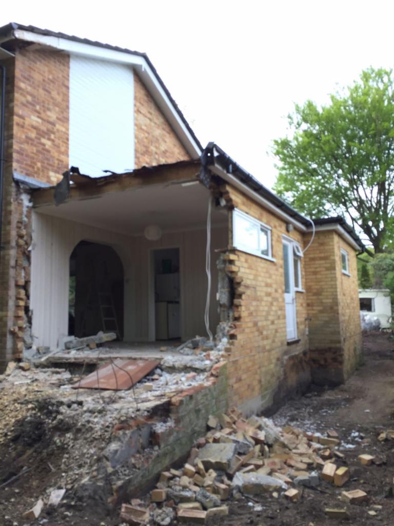 Częściowo zdemontowana ściana zewnętrzna domu z cegły, widoczne gruzy i odsłonięte wnętrze, przygotowanie do rozbudowy.