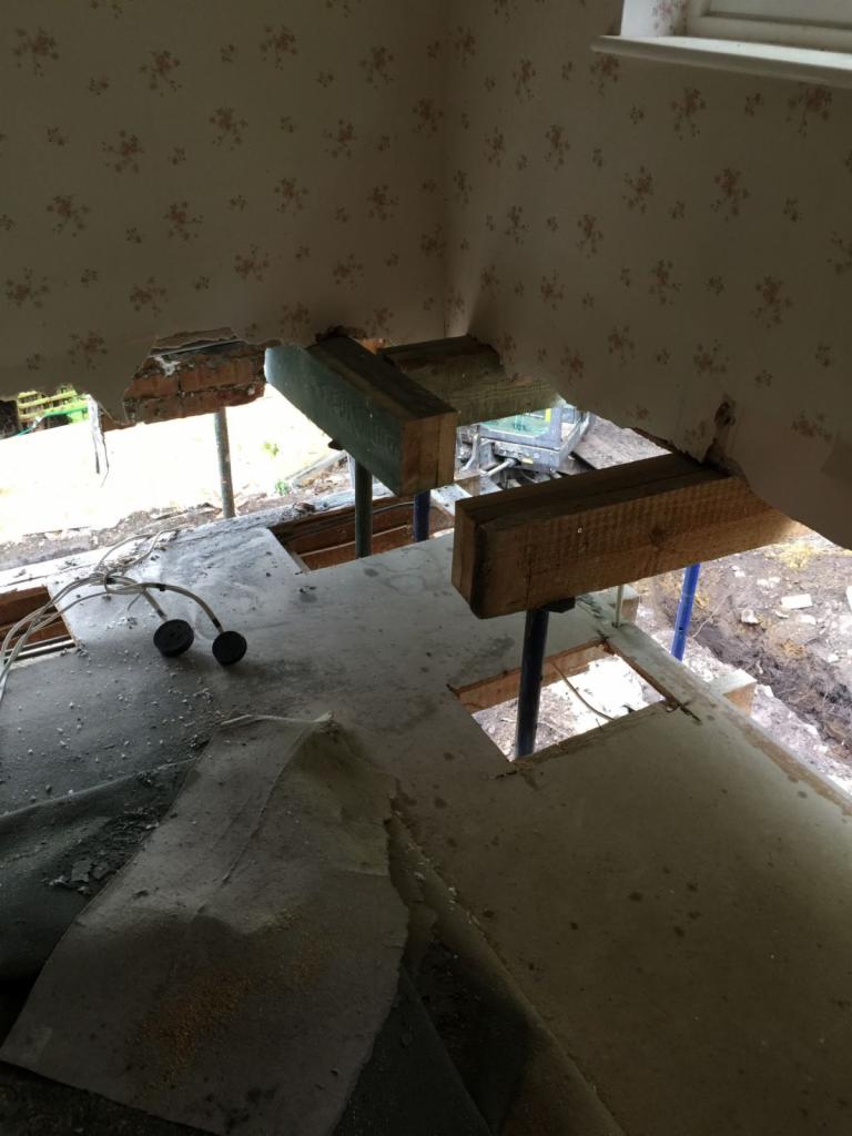 Demontaż fragmentu ściany i stropu podczas prac budowlanych, widoczne drewniane podpory tymczasowe i wystające kable.