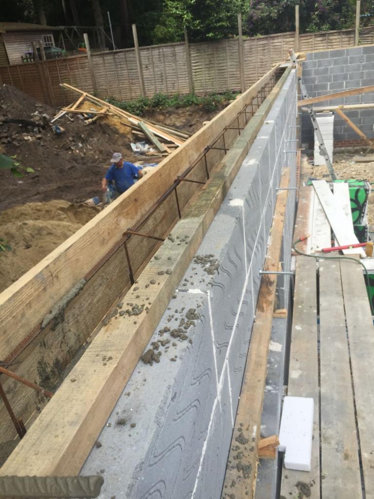 Wznoszenie ściany z szalunków traconych z betonu komórkowego, widoczne zbrojenie i pracownik w tle.