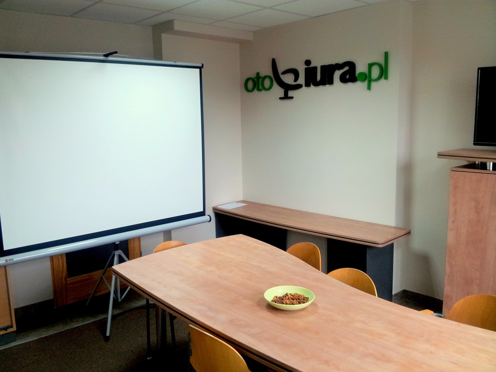Sala konferencyjna z projektorem, stołem z przekąskami i logo firmy na ścianie.