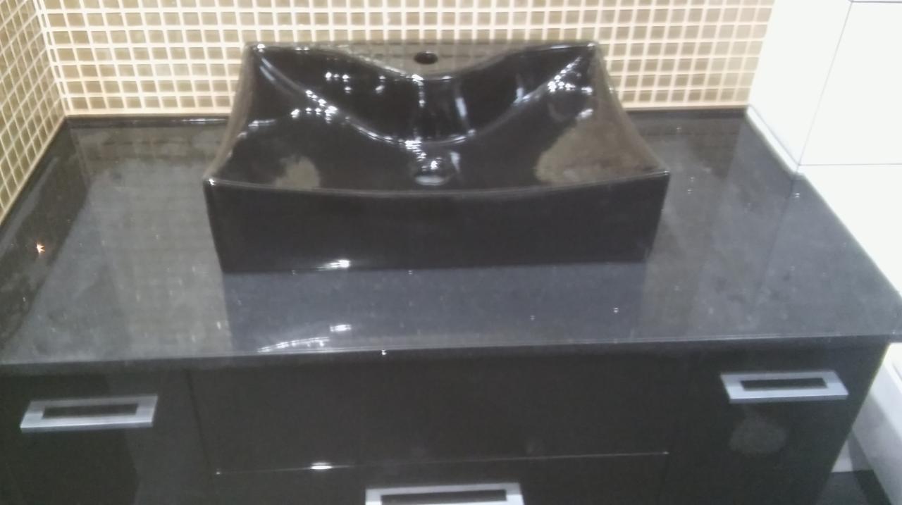 Czarna, kwadratowa umywalka nablatowa na czarnym blacie z szafką, z minimalistycznymi, prostokątnymi uchwytami, na tle mozaiki z beżowych płytek.