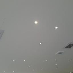 F.U.Arek Arkadiusz Wielosz - Kasetonowe jednostki sufitowe w biurze, jedna z nich z częściowo zdjętą folią ochronną, w tle liczne wpuszczane lampy punktowe.