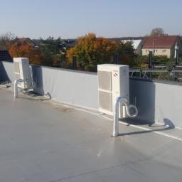 F.U.Arek Arkadiusz Wielosz - Dwa moduły zewnętrzne klimatyzacji zamontowane na płaskim dachu budynku z szarym wykończeniem, widoczne rury odprowadzające skropliny, w tle zabudowa jednorodzinna i drzewa z jesiennymi liśćmi.