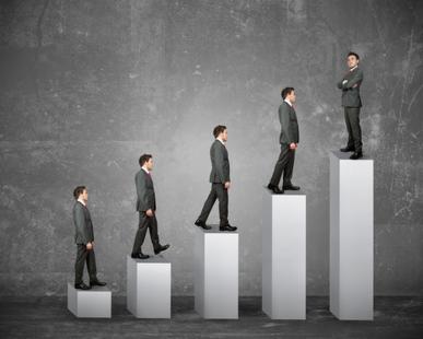 Mężczyzna w garniturze wspinający się po białych blokach symbolizujących wzrost, coaching dla sprzedawców.