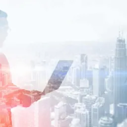 Sylwetka mężczyzny z laptopem na tle panoramy miasta z efektem podwójnej ekspozycji, gdzie w sylwetce widoczne są budynki.