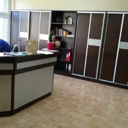 Biuro z recepcją, za którą siedzi pracownik, w tle zabudowa meblowa z przesuwnymi drzwiami i regałami.