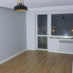 Pusty pokój po malowaniu i położeniu paneli podłogowych, widok na okno z widokiem na nocne miasto, nowoczesna lampa wisząca.