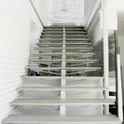 Nowoczesne schody z betonu architektonicznego z białymi wspornikami, umieszczone przy białej ścianie z cegły, oświetlone naturalnym światłem z okna.