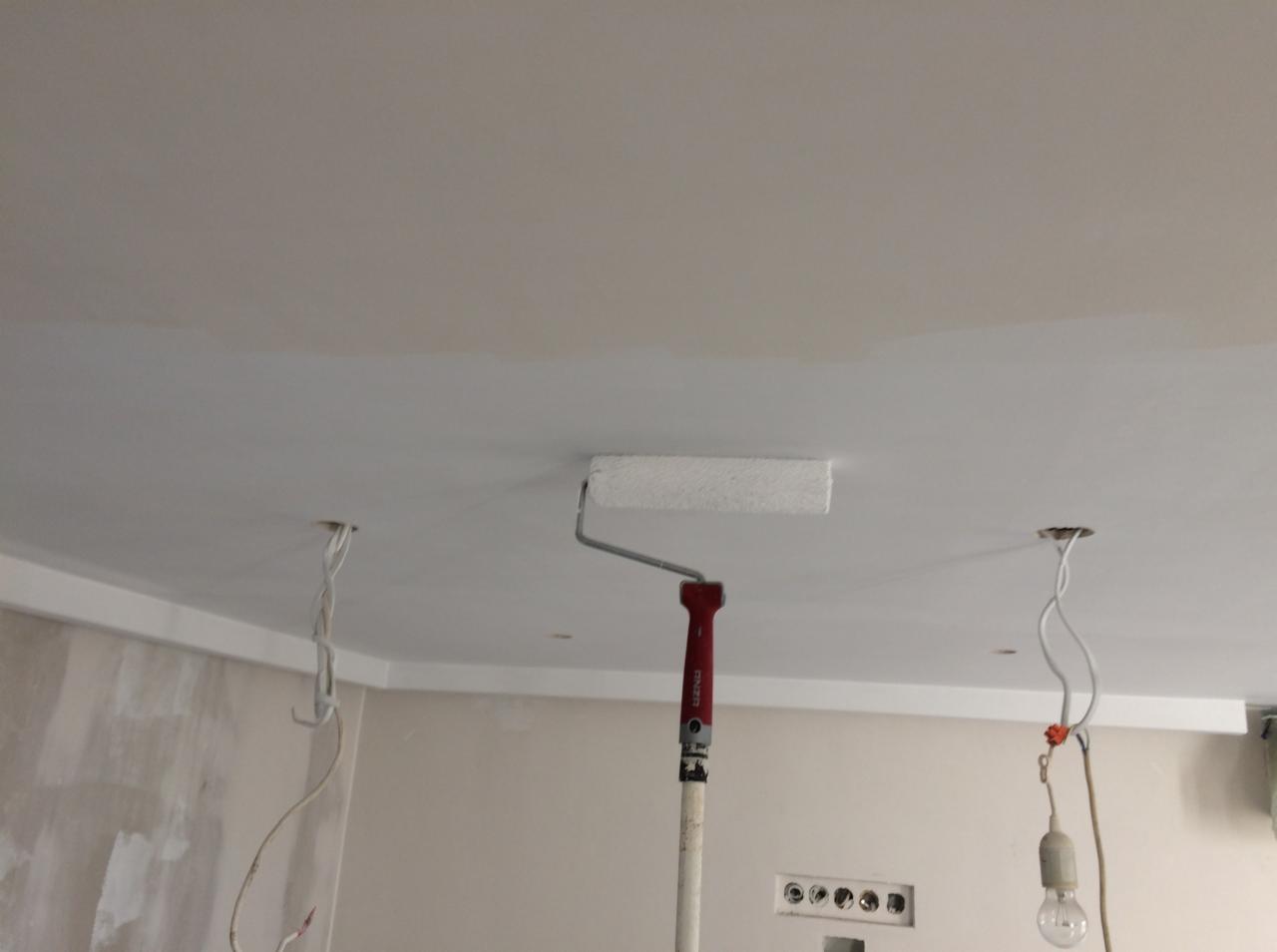 Malowanie sufitu wałkiem na teleskopowym kiju, widoczne przewody elektryczne wystające z sufitu, ściany przygotowane pod malowanie.