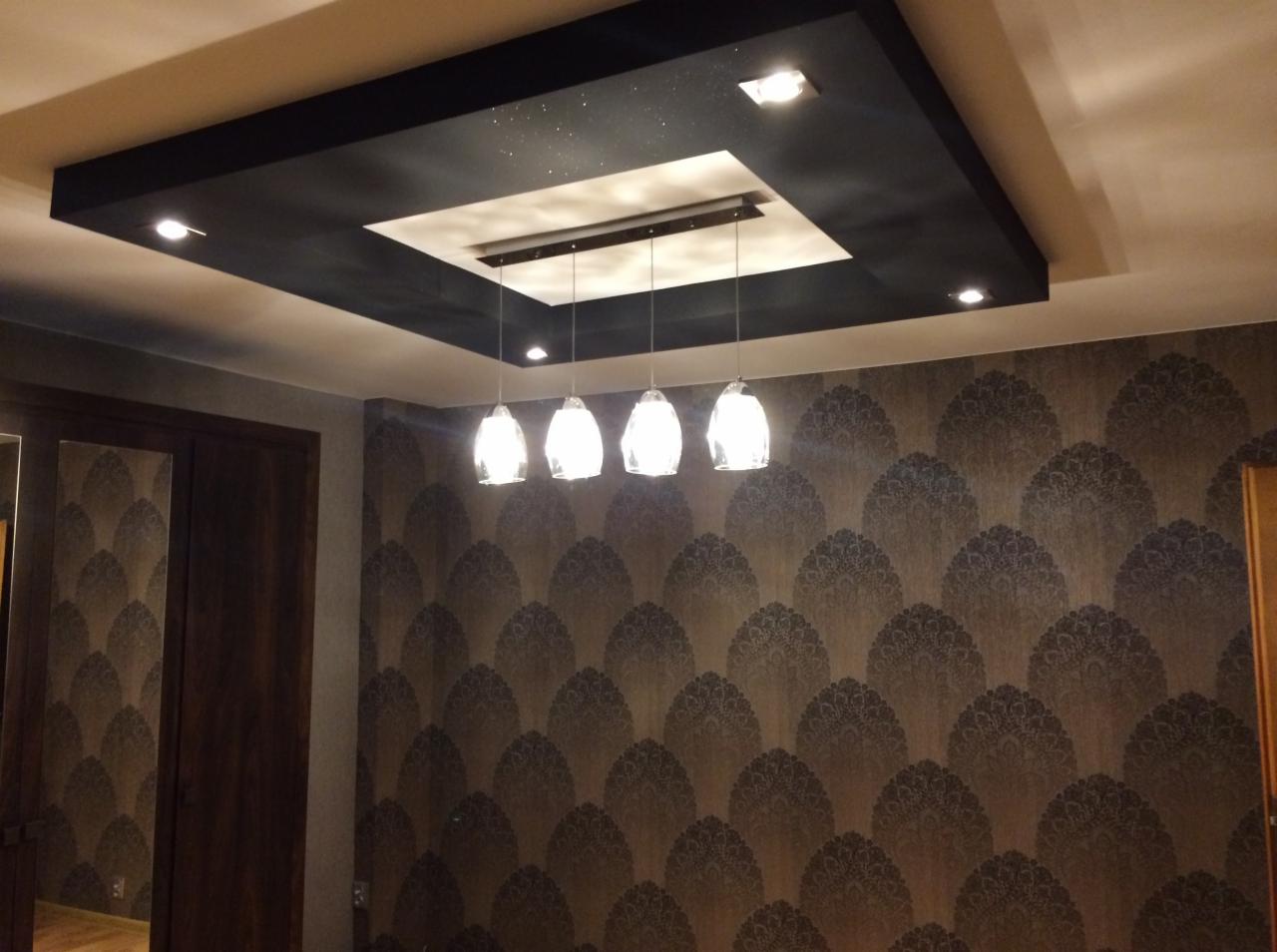 Czarny podwieszany sufit z efektem gwiazd, oświetleniem punktowym i czterema szklanymi lampami wiszącymi nad wzorzystą tapetą w odcieniach brązu.