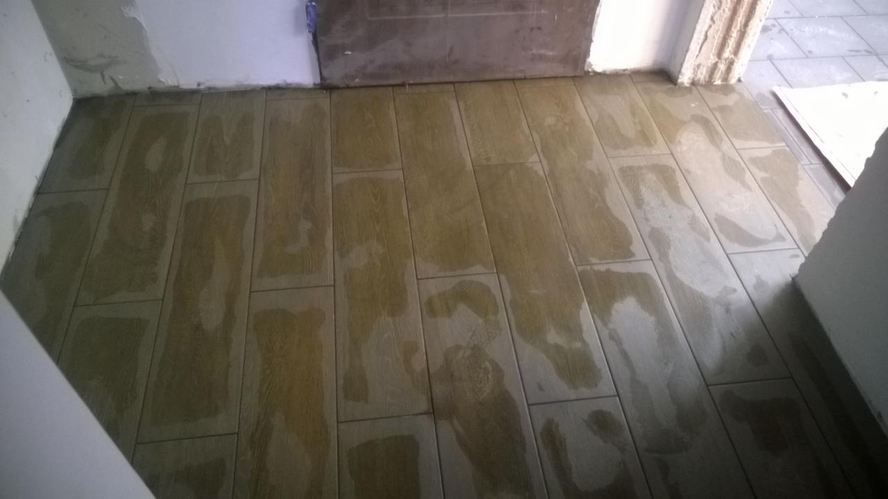 Ułożone, mokre panele podłogowe imitujące drewno, widoczne niedociągnięcia przy ścianach i futrynie drzwi.