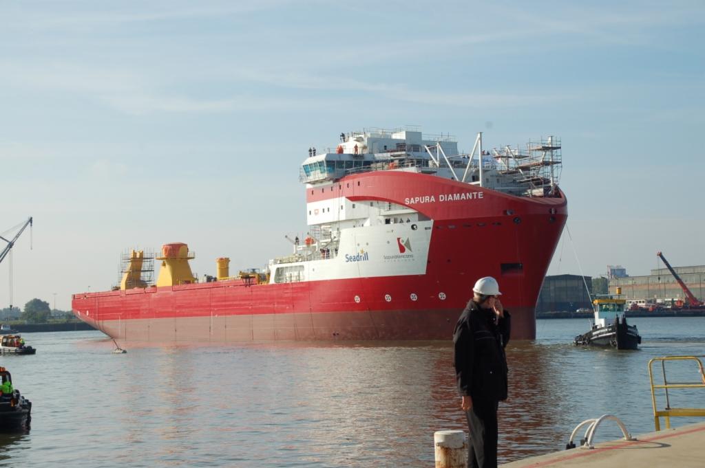 Czerwono-biały statek Sapura Diamante na wodzie, z mężczyzną w kasku rozmawiającym przez telefon na pierwszym planie.