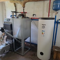 Instal P&P - Kotłownia z piecem na paliwo stałe Stalmark z podajnikiem ślimakowym, zasobnikiem ciepłej wody Kospel i instalacją hydrauliczną w surowym pomieszczeniu.