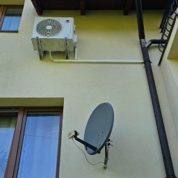 Instal P&P - Zewnętrzna jednostka klimatyzacji zamontowana na elewacji domu obok okna i rynny, widoczna także antena satelitarna.