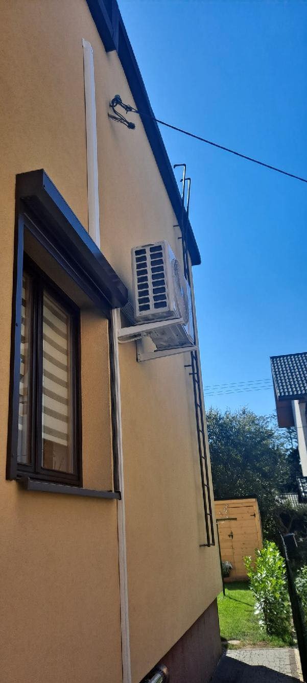 Klimatyzator zewnętrzny zamontowany na elewacji domu w Babicy, widoczna instalacja odprowadzająca skropliny.