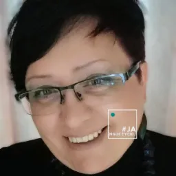 Portret uśmiechniętej kobiety w okularach, z krótkimi ciemnymi włosami i hasztagiem #JANauczyciel w prawym dolnym rogu kadru.