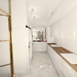 IZA ROJSZA - Wąska, jasna kuchnia z białymi szafkami i drewnianym blatem, widok w głąb pomieszczenia z perspektywy szklanej ścianki działowej z złotymi ramami, marmurowa podłoga.
