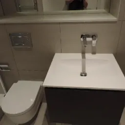 Nowoczesna łazienka z wiszącą toaletą, umywalką nablatową na szafce w kolorze antracytowym i armaturą chromowaną, widok z perspektywy pod lekkim kątem.