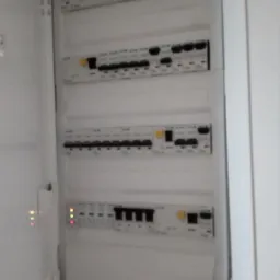 Otwarta skrzynka rozdzielcza z widocznymi bezpiecznikami i włącznikami, niektóre z diodami sygnalizacyjnymi włączonymi.