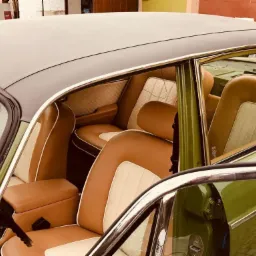 Wnętrze odrestaurowanego klasycznego samochodu z brązowo-kremową tapicerką, widok z otwartych drzwi na fotele i tylną kanapę z pikowanymi wstawkami.