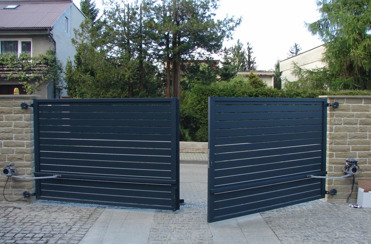 Szara, pozioma brama przesuwna z napędem, otwarta w połowie, zamontowana na kamiennym murku, widok z zewnątrz posesji.
