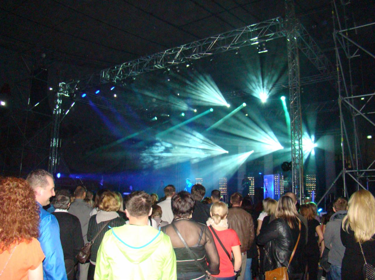 Widok na scenę z publicznością podczas koncertu z efektami świetlnymi i konstrukcją stalową.