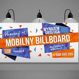 Ilustracja mobilnego billboardu LED z napisem 'Wyróżnij się!', 'Wynajem Obsługa', 'skuteczna reklama' i numerem telefonu, oświetlonego trzema reflektorami, na szarym tle.