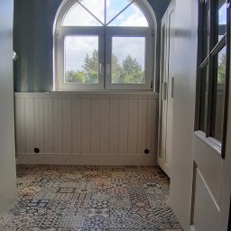 Dariusz Pawełek SilvaDeco - Jasne wnętrze z okrągłym oknem, wzorzystą podłogą i panelami ściennymi. Widok z drewnianej podłogi na płytki i okno z widokiem na zieleń.