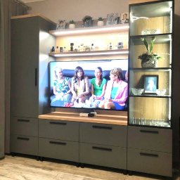 MEB-MAR - Szara zabudowa meblowa z drewnianymi akcentami, oświetleniem LED i szklaną witryną, z telewizorem wkomponowanym w centralną część. Nowoczesny design.