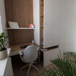 MEB-MAR - Nowoczesny pokój z biurkiem z drewnianym blatem, białą szafą wnękową i ścianą z drewnianych lameli. Rośliny doniczkowe dodają wnętrzu świeżości.