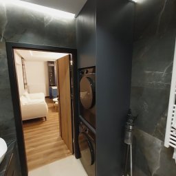 MEB-MAR - Nowoczesna zabudowa łazienkowa z pralką i suszarką w kolumnie, ciemnoszara szafa z ryflowanym frontem, marmurowe ściany, widok na salon przez otwarte drzwi.