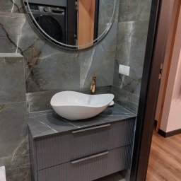 MEB-MAR - Nowoczesna łazienka z umywalką nablatową w kształcie łzy, szafką z frezowanymi frontami i lustrem. Marmurowe płytki na ścianach i złota bateria.