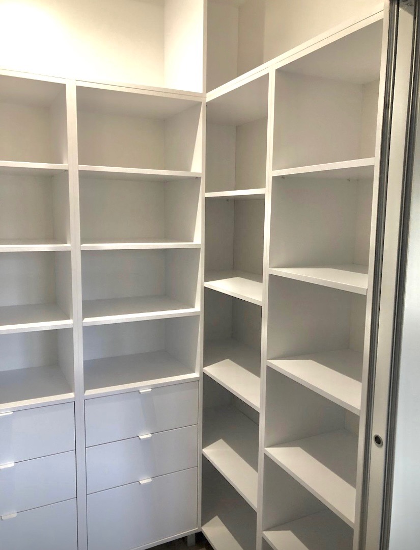 Biała szafa wnękowa z półkami i szufladami, widok z wnętrza. Minimalistyczny design, jasne oświetlenie, drzwi przesuwne po prawej stronie.