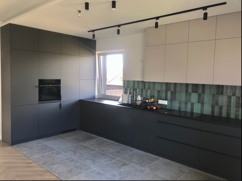 Nowoczesna kuchnia z szarymi i beżowymi szafkami, czarnym blatem i zieloną mozaiką nad zlewem. Oświetlenie szynowe. Minimalistyczny design.