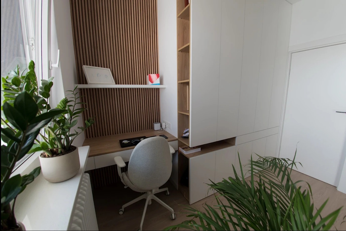 Nowoczesny pokój z biurkiem z drewnianym blatem, białą szafą wnękową i ścianą z drewnianych lameli. Rośliny doniczkowe dodają wnętrzu świeżości.