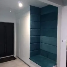 Wnęka z siedziskiem obita turkusowym, pikowanym materiałem, zintegrowana z białą szafą w przedpokoju, oświetlona punktowo.